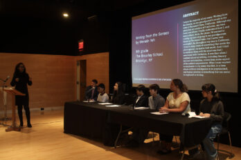 Woman speaking in front a panel of writers